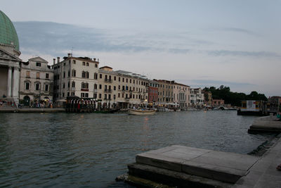 Buildings at waterfront against cloudy sky