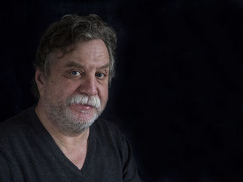 Close-up of smiling mature man against black background