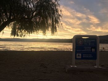 Information sign on beach against sky during sunset