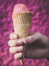 Cropped hand of boy holding ice cream cone against wall