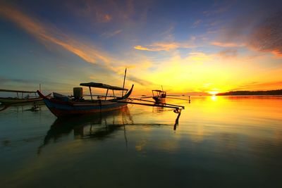 Silhouette boat moored on sea against sky during sunset