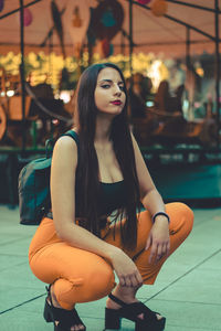 A brunette girl sitting and looking at camera with a carousel as background