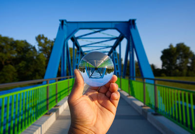 Person holding umbrella on bridge against blue sky