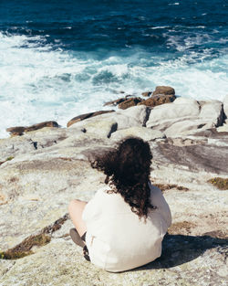 Rear view of woman sitting on rock at beach