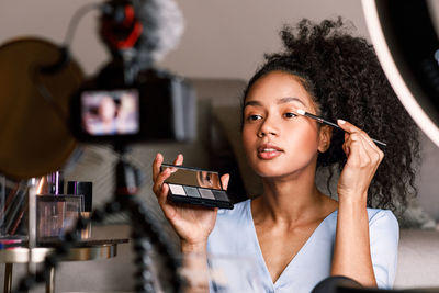 Smiling young woman applying face powder by camera at home