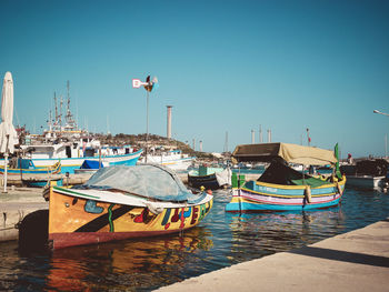 Boats moored at harbor against clear blue sky