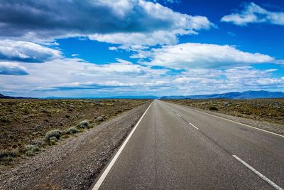 Street amidst field against cloudy sky