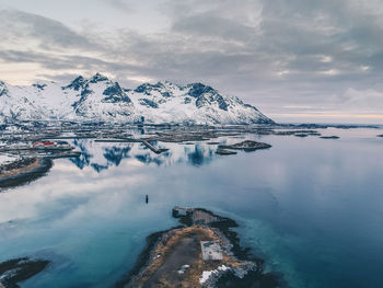 Scenic view of sea by snowcapped mountains against cloudy sky