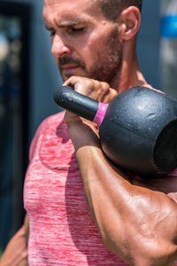 Serious male athlete with strong body doing exercises with heavy metal kettlebell during intense workout in summer