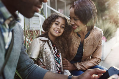 Happy mother looking at daughter while sitting by man during sunny day