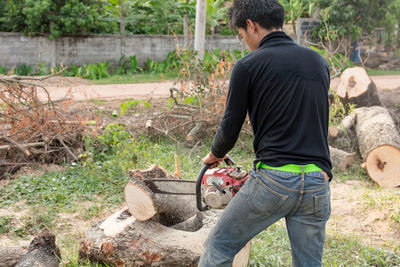 Rear view of young man cutting log in forest