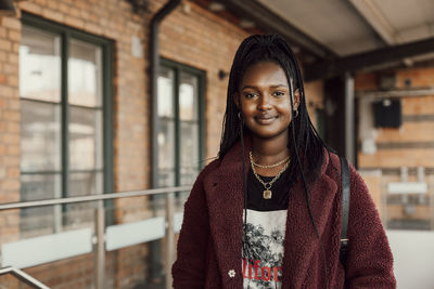Portrait of smiling young woman standing against brick wall