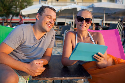 Happy couple looking in digital tablet while relaxing at beach