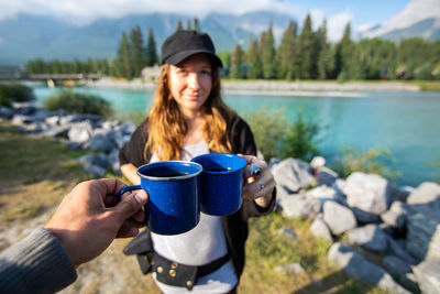 Young woman holding coffee cup by lake