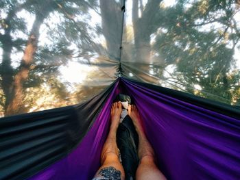 Low section of man relaxing in hammock against trees