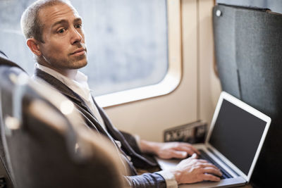 Mature businessman looking away while using laptop in train