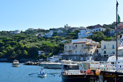 Sailboats moored on harbor by buildings in city against clear sky