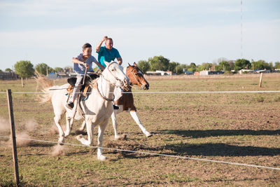 Men riding horse on field against sky