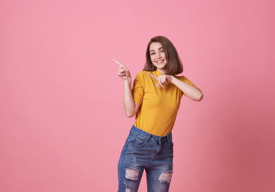 Portrait of young woman holding umbrella standing against pink background