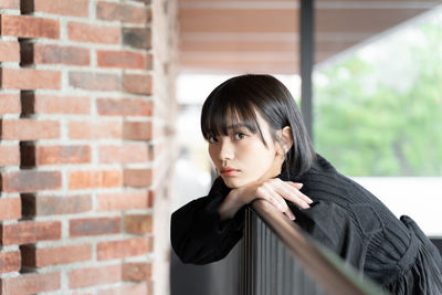 Close-up of young woman standing against brick wall