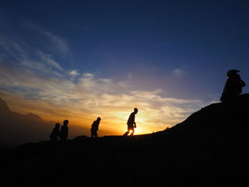 Silhouette people standing on land against sky during sunset