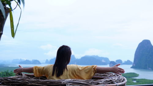 Rear view of woman sitting on rock against sky