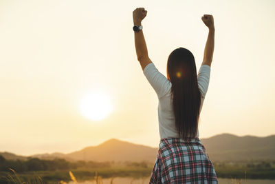 Rear view of woman standing against sky during sunset