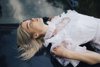 Woman lying on the hood of a car in a white dress