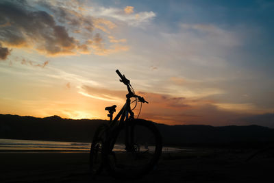 Silhouette bicycle on beach against sky during sunset