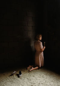 Full length of woman holding candle sitting by wall indoors