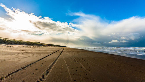 Tire track on beach against sky