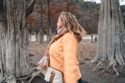 Side view of woman standing on tree trunk