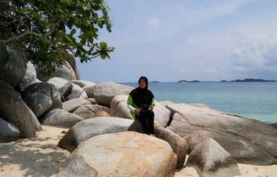 Woman sitting on rock by sea against sky