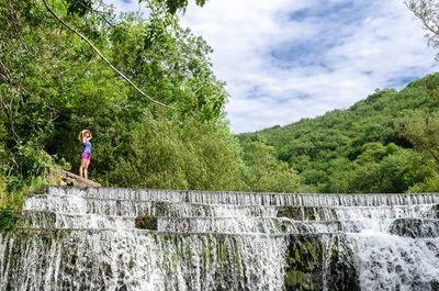 Woman standing by waterfall against trees