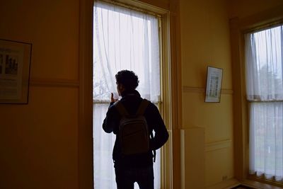 Rear view of man looking through window at home