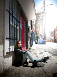 Full length portrait of woman sitting by building