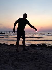 Silhouette man standing on beach against sky during sunset