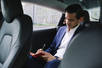 Businessman sitting in electric car writing on diary