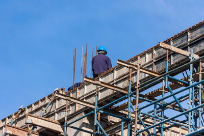 Low angle view of man working at construction site against blue sky