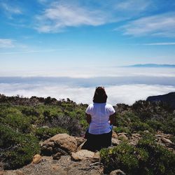 Rear view of woman sitting on rock against sky