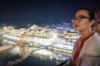 Woman looking at illuminated city against sky at night