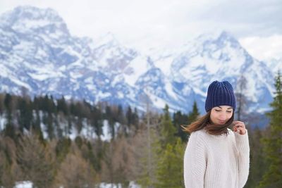 Young woman in warm clothing standing against snowcapped mountain