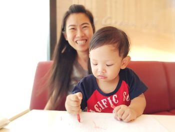 Boy drawing on paper while sitting with mother at home