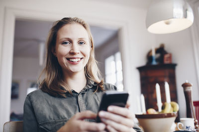 Low angle portrait of young woman using mobile phone at home