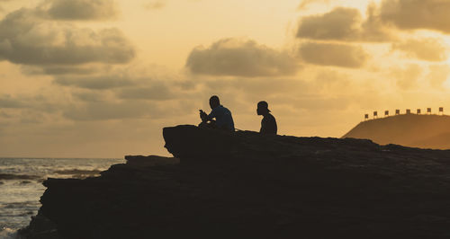 Silhouette rock on beach against sky during sunset