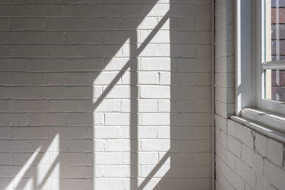 Sunlight and hard shadows from window against white brick wall in corner of room