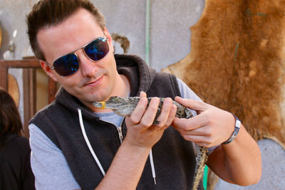 Man in sunglasses holding crocodile against wall