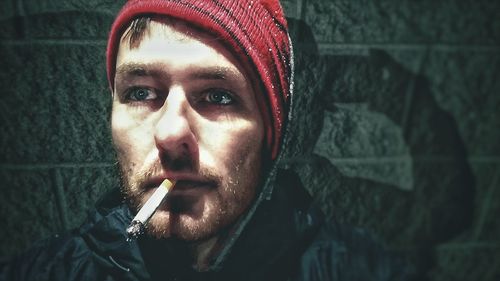 Close-up of man smoking cigarette against wall at night