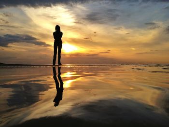 Reflection of silhouette woman on beach against sky during sunset