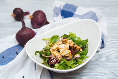 Deep bowl of arugula salad with cheese and chicken fillet slices. dressed with balsamic sauce.